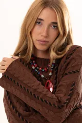 Buzo de tejido de punto color chocolate con diseño de trenzas verticales y detalles de costuras en contraste color negro. Presenta cuello redondo, mangas largas con terminación acampanada y aberturas laterales en el ruedo.