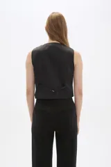 Chaleco negro sin mangas con escote en V y cierre frontal con botones. Diseño corto con solapas simuladas a la altura de la cintura.