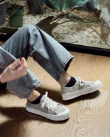 Zapatillas urbanas de lona color beige con cordones blancos y suela de goma blanca con diseño geométrico.