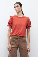 Remera de algodón color terracota con cuello redondo y mangas cortas con detalle de volados escalonados y costuras decorativas.
