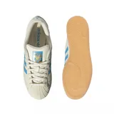Championes Adidas Superstar edición especial Messi, color crema con las icónicas tres tiras en azul celeste. Presenta el logo de Messi grabado en el lateral y en el talón, con la clásica puntera de goma y suela de color goma.