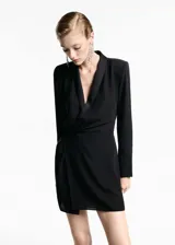 Vestido corto de color negro con diseño cruzado, cuello en pico con solapa tipo blazer y manga larga. Presenta un lazo en la cintura que permite ajustar la prenda y un tejido fluido y ligero con forro interior.