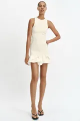 Vestido corto de color blanco con cuello redondo y diseño sin mangas. Presenta un cuerpo de tejido bouclé texturizado y un bajo acabado con volantes de tejido ligero.