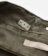 Pantalón flare de sarga color verde oliva, con cintura ancha, doble botón, cierre tradicional, trabillas, detalle de recortes y bolsillos.