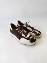 Zapatilla deportiva de cuero con estampado de vaca (pelo), color marrón y blanco. Suela blanca gruesa.