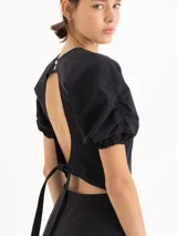 Vestido corto negro de popelina elastizada, con cuello redondo, mangas cortas abullonadas con volumen y falda evasé estructurada.