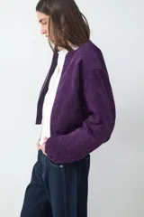 Campera bomber corta de pana color violeta, con cierre frontal de cremallera, cuello redondo y mangas largas con puños elásticos.