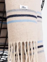 Bufanda de tejido suave en color marrón chocolate con diseño de rayas horizontales en tonos naranja, beige y gris. Presenta terminaciones con flecos en los extremos.