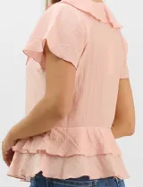 Blusa de satén color rosado con acabado texturizado, escote en V con volados, mangas cortas acampanadas y diseño péplum de doble nivel en la parte inferior.