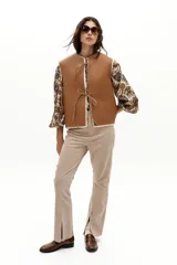 Chaleco reversible de gamulán de oveja en color natural, con corte holgado, cuello a la base y terminaciones al corte. Presenta tiras de cuero en el frente para atar.