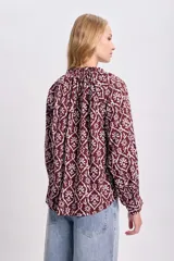 Blusa de estilo boho color bordó con estampado floral blanco, cuello redondo con cordones ajustables y mangas largas abullonadas con puños elásticos.