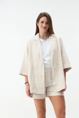 Blazer negro de corte recto y holgado, con doble botonadura frontal, solapas clásicas y mangas tres cuartos con costuras pespunteadas en contraste.