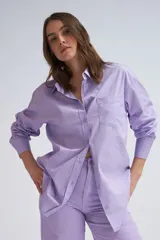 Camisa oversize color lavanda de poplin con cuello clásico, cierre frontal con botones, manga larga con puños abotonados y bolsillo de parche en el pecho.
