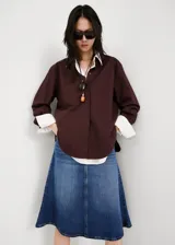 Falda midi evasé de denim estilo vaquero, con tiro medio, trabillas, diseño de cinco bolsillos y cierre frontal con botón y cremallera.