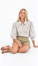 Camisa clásica de lino natural color blanco, con mangas abullonadas tres cuartos y delicados bordados artesanales de flores en el frente.