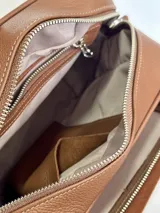 Bandolera marrón de cuero genuino con textura tipo cocodrilo en el frente. Tiene correa de tela con el nombre de la marca y herrajes plateados.