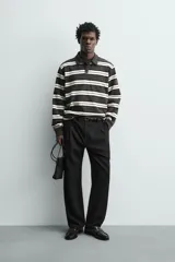 Polo de manga larga con diseño de rayas horizontales en tonos gris oscuro, negro y blanco marfil, cuello solapa y cierre frontal de botonadura oculta.