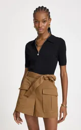 Remera de punto acanalado color negro, con silueta ajustada, cuello polo estructurado, mangas cortas y cierre frontal con cremallera metálica y colgante decorativo.