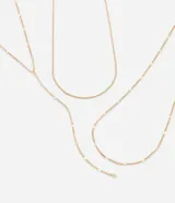 Collar triple de metal dorado con diseño en capas, compuesto por cadenas finas de diferentes largos y un detalle frontal estilo corbata con caída alargada y pequeño dije esférico.