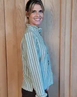 Camisa de manga larga con estampado de rayas verticales en tonos crudo y beige. Presenta cuello alto con volados, cierre frontal con botones dobles y puños con volados.