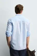 Camisa regular fit de manga larga con diseño a rayas verticales celestes y blancas. Cuenta con cuello abotonado, bolsillo de parche en el pecho y cierre frontal con botones.