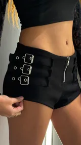 Short de tiro bajo en color negro, confeccionado en material engomado. Presenta un cierre frontal metálico y tres correas laterales decorativas con hebillas plateadas.