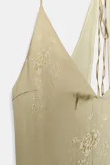 Vestido midi lencero con escote pico y tirantes finos ajustables con lazada en la espalda. Presenta un efecto degradado de color, pasando de un tono beige/amarillento claro en la parte superior a un verde azulado oscuro en el bajo. El tejido tiene un estampado sutil de rosas en relieve.