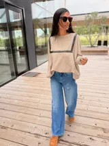 Sweater de tejido de punto en color beige, con corte holgado y diseño de cuello redondo. Presenta apliques decorativos de cuero en la parte frontal superior, formando un detalle geométrico.