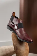 Zapato tipo botineta de cuero color bordó con textura grabada, diseño de punta fina y detalles de elásticos laterales en color negro.