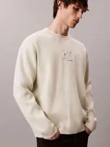 Sweater de punto color beige con cuello redondo, mangas largas y corte regular. Cuenta con el logo distintivo de Calvin Klein bordado en relieve al tono en el pecho.
