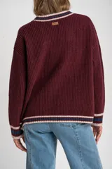 Cardigan de punto color bordó con diseño oversize, cuello en V y cierre frontal con botones. Presenta detalles de rayas en contraste en color crema y azul en los bordes, puños y ruedo, además de dos bolsillos frontales aplicados.