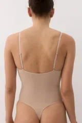Body modelador tipo tanga color beige, con efecto vientre plano. Presenta copas forradas con sección en punto menguado para realce y sujeción suave, sin aros. Cuenta con breteles ajustables y cierre inferior con botones a presión ocultos. Diseño sin costuras para mayor comodidad.