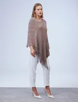 Poncho tejido en hilo soft, con efecto jaspeado multicolor (predominantemente tonos oscuros como azul marino, negro, y toques de violeta y dorado/lurex). Presenta un diseño asimétrico y flecos largos en los bordes.