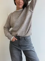 Sweater de punto de corte holgado en color gris melange, con cuello redondo y puños acanalados que presentan un detalle de contraste en color blanco. Posee mangas tipo raglán y una textura suave y elástica.