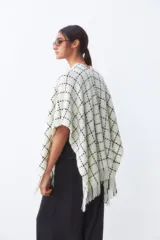 Ruana de tejido de punto con diseño a cuadros en color blanco y negro, con terminación de flecos en el ruedo.