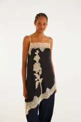 Blusa de breteles finos de color negro, con silueta amplia y caída asimétrica, confeccionada en tejido liviano con delicados detalles de encaje floral en el escote y el ruedo, y un gran aplique de encaje con diseño floral vertical en el frente.