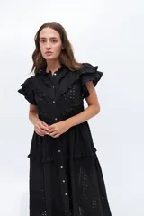 Vestido midi de lino blanco con diseño de broderie, cuello alto, cierre frontal con botones y volados decorativos en los hombros y el cuerpo.