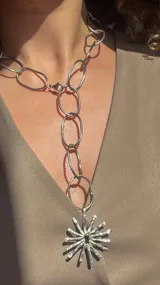 Collar plateado con cadena de eslabones ovalados y dije en forma de sol con centro negro.