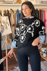 Buzo de punto negro con diseño de flores bordadas en hilo blanco, cuello redondo y mangas largas con puños acanalados.