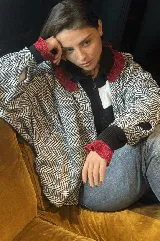 Campera bomber oversize de paño italiano con estampado en zigzag blanco y negro, cuello alto y cierre frontal con broches a presión. Tiene mangas murciélago.