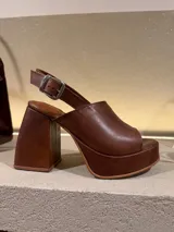 Sandalia de plataforma y taco alto, color beige claro con textura de piel de reptil. Presenta una capellada ancha que cubre los dedos y el empeine, y una tira ajustable con hebilla metálica en el tobillo.