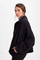 Campera holgada de felpa color gris, con cuello alto, cierre frontal completo, mangas tipo murciélago y bolsillos laterales.