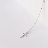 Pulsera tipo denario confeccionada en plata 925, compuesta por una cadena fina con pequeñas esferas intercaladas y un dije colgante en forma de cruz.