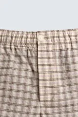 Bermuda de hombre, corte relajado, color beige con estampado de cuadros en tonos marrones y rosados. Presenta cintura elástica, bolsillos frontales y un bolsillo trasero de plastrón con cierre de botón.