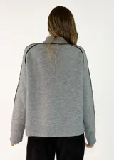 Sweater de punto gris con cuello alto y detalles de líneas negras contrastantes en los hombros y mangas. Presenta puños y ruedo acanalados.