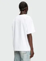 Remera blanca de corte holgado con cuello redondo y manga corta. Presenta un pequeño parche rectangular rojo con el logo de Diesel en el pecho.