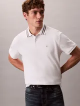 Chomba de piqué blanca Calvin Klein, de corte regular y manga corta, con cuello clásico con líneas grises en contraste y cartera de dos botones. Cuenta con el monograma CK bordado discretamente en el pecho.