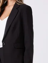 Blazer sastrero negro de corte entallado, con cuello de solapa, hombreras, cierre frontal con un botón y bolsillos laterales con solapa.