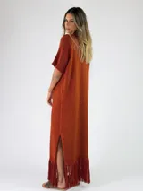 Vestido largo bordó de punto metalizado, con escote en V, mangas cortas y detalle de flecos en el ruedo.