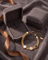 Pulsera de acero con baño de oro, diseño de cadena de malla flexible y tres dijes circulares decorados con nácar, ónix y circonias pavé.